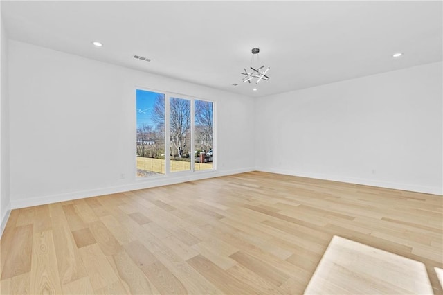 spare room with baseboards, light wood-type flooring, visible vents, and an inviting chandelier