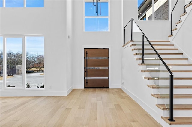 entryway featuring light wood-type flooring, baseboards, a high ceiling, and stairs