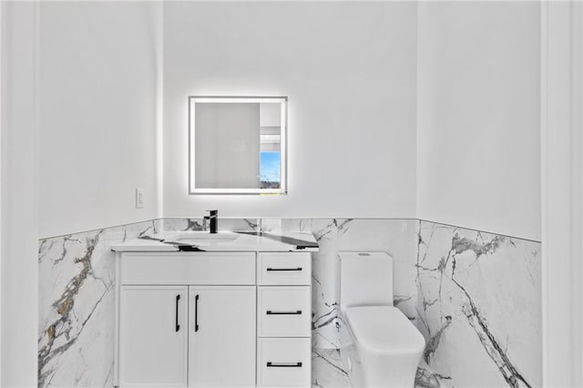 bathroom featuring toilet, a wainscoted wall, tile walls, and vanity