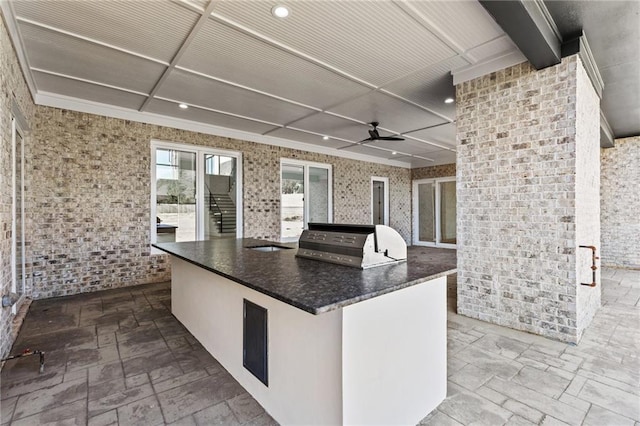 kitchen with stone tile floors, white cabinets, brick wall, ceiling fan, and a large island with sink