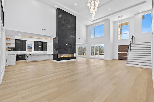 living area featuring light wood-style flooring, stairs, a multi sided fireplace, a notable chandelier, and recessed lighting