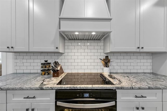 1021 Windsor Creek Dr, Madison, GA 30650 - kitchen with premium range hood, wall oven, black electric stovetop, backsplash, and white cabinetry