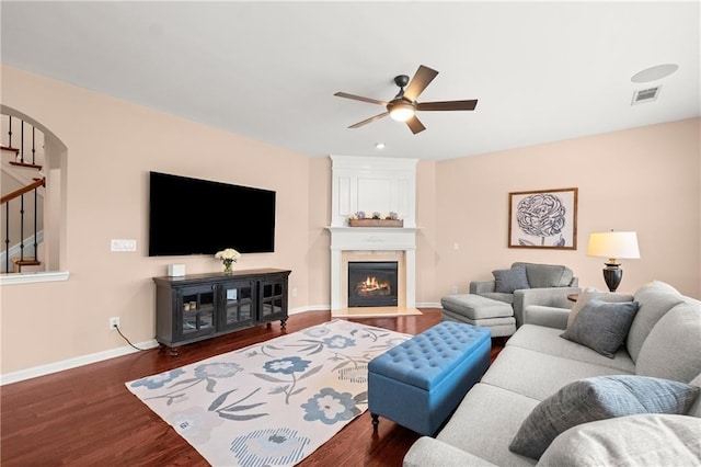 living room with dark wood-type flooring, ceiling fan, and a large fireplace