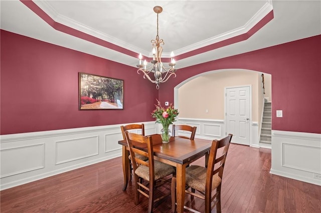 dining area with dark wood-type flooring, ornamental molding, a raised ceiling, and an inviting chandelier