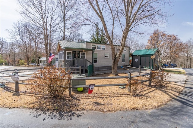 view of front of property featuring a fenced front yard, metal roof, a storage shed, and an outbuilding