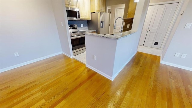 kitchen featuring kitchen peninsula, backsplash, stainless steel appliances, sink, and light hardwood / wood-style floors