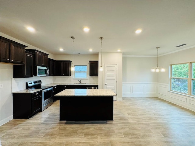 kitchen with sink, a center island, light stone counters, decorative light fixtures, and appliances with stainless steel finishes