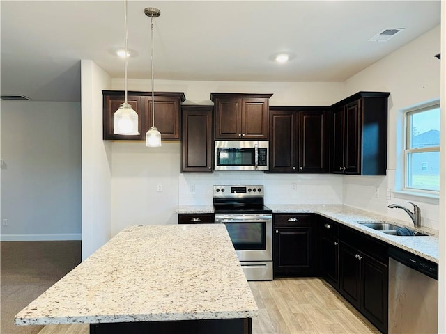 kitchen featuring sink, a center island, stainless steel appliances, pendant lighting, and light wood-type flooring