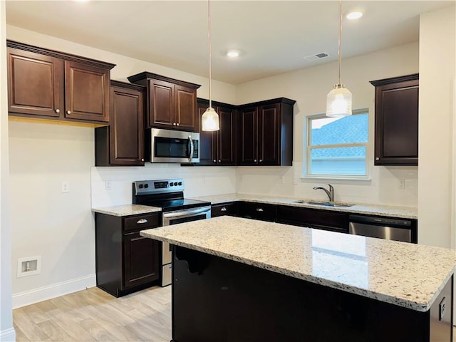 kitchen featuring sink, light hardwood / wood-style floors, decorative light fixtures, and appliances with stainless steel finishes