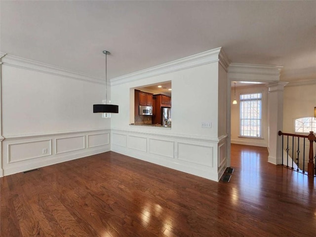 unfurnished living room featuring visible vents, dark wood-style floors, ornamental molding, ornate columns, and a decorative wall