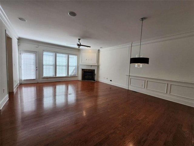 unfurnished living room featuring dark wood-style floors, ornamental molding, a fireplace, and a ceiling fan