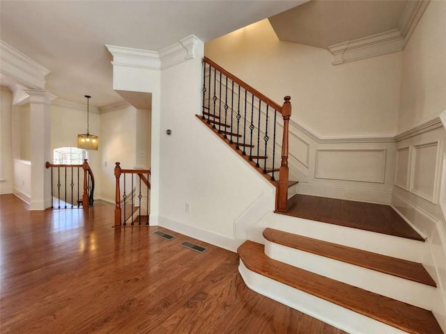 stairway featuring a decorative wall, wood finished floors, visible vents, and crown molding