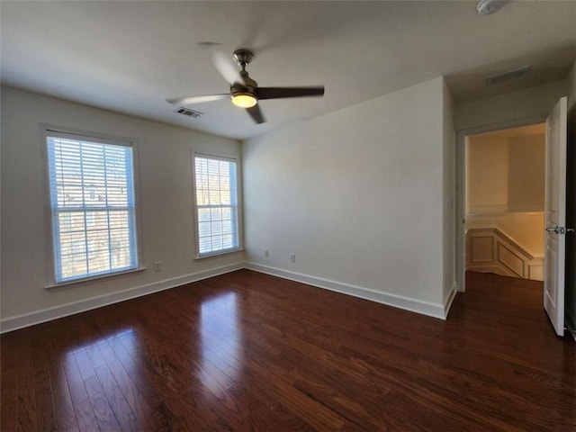 empty room with dark wood-style flooring, visible vents, and baseboards