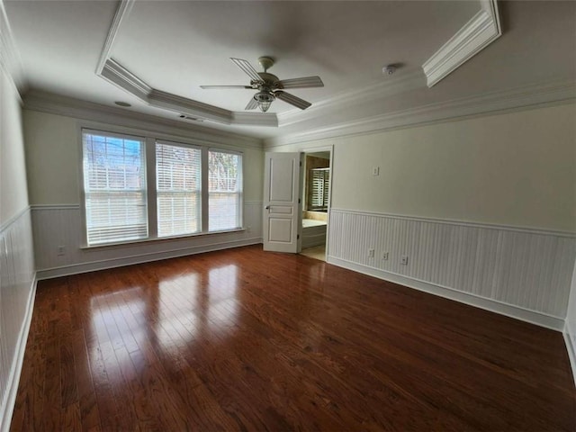 empty room with a wainscoted wall, wood-type flooring, visible vents, a raised ceiling, and a ceiling fan