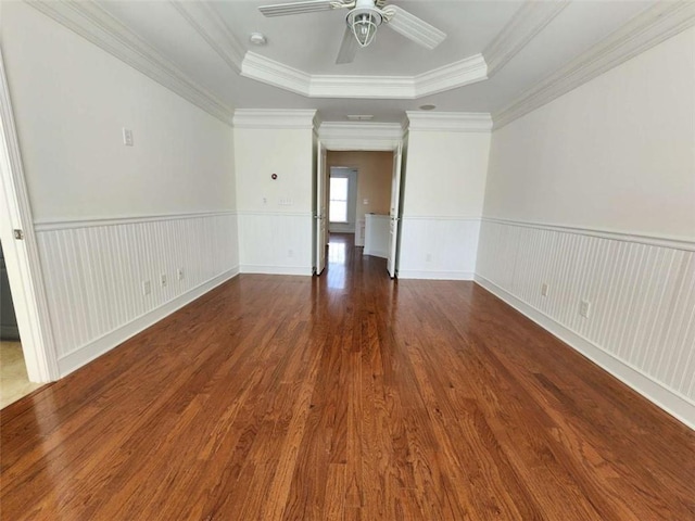 unfurnished room with a tray ceiling, wainscoting, wood finished floors, and a ceiling fan