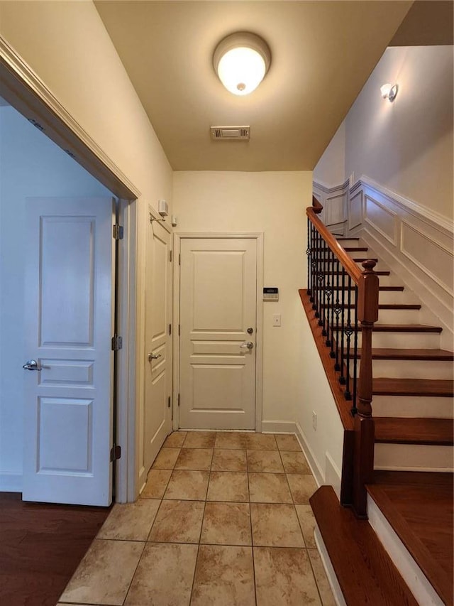 interior space with light tile patterned floors, a decorative wall, visible vents, stairs, and wainscoting