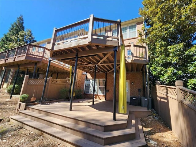 rear view of property featuring brick siding, fence, and a wooden deck