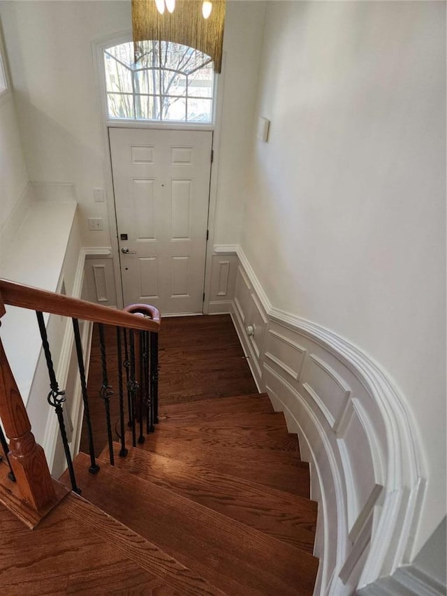 staircase with a decorative wall, wood finished floors, and wainscoting