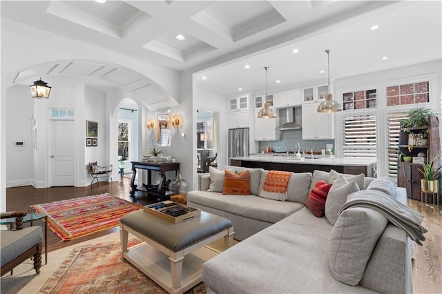 living room featuring light wood-style floors, plenty of natural light, arched walkways, and coffered ceiling