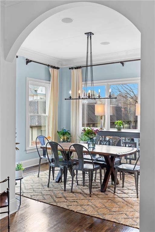 dining space with arched walkways, a notable chandelier, crown molding, wood finished floors, and baseboards