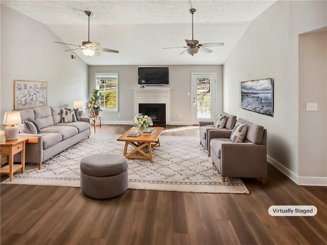 living area featuring lofted ceiling, ceiling fan, a fireplace, wood finished floors, and baseboards