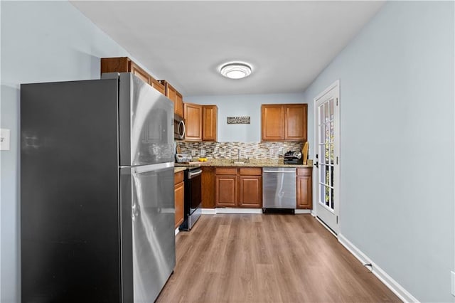 kitchen featuring light stone counters, brown cabinets, stainless steel appliances, light wood-style flooring, and backsplash