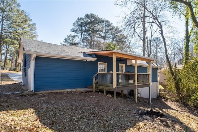 back of house featuring roof with shingles, fence, and a deck