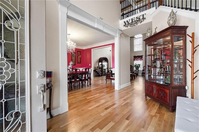 foyer with a notable chandelier, a high ceiling, light wood-style floors, ornamental molding, and stairs