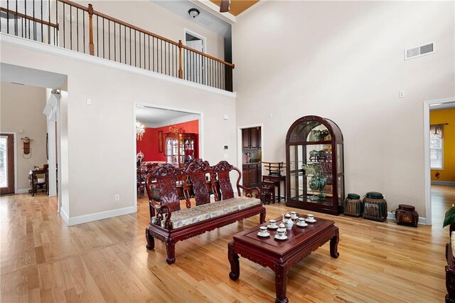 living area with a towering ceiling, light wood-style flooring, visible vents, and baseboards