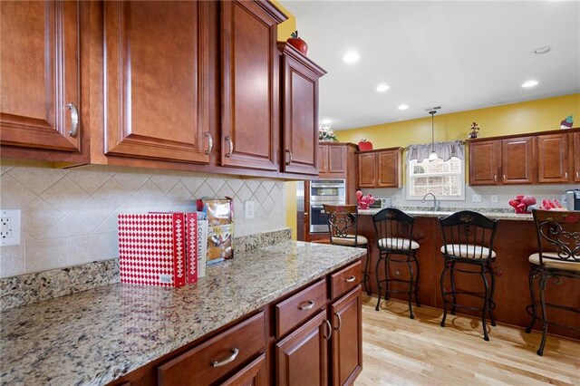 kitchen with light stone counters, pendant lighting, light wood finished floors, decorative backsplash, and a sink