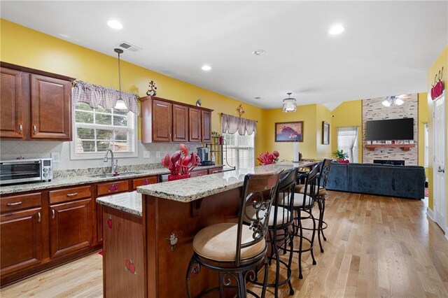 kitchen featuring tasteful backsplash, open floor plan, a center island, hanging light fixtures, and a sink