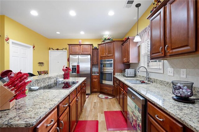 kitchen featuring light stone counters, visible vents, hanging light fixtures, appliances with stainless steel finishes, and a sink