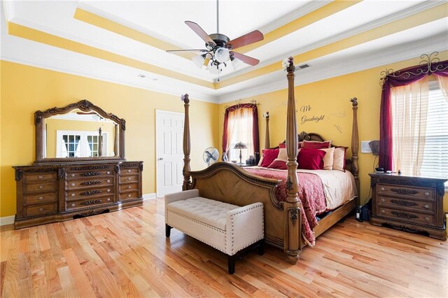 bedroom featuring light wood-style floors, a tray ceiling, and multiple windows