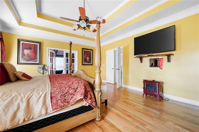 bedroom with french doors, crown molding, light wood finished floors, a raised ceiling, and a wood stove