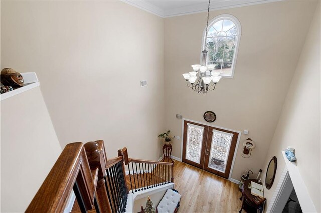 entryway featuring baseboards, light wood-style flooring, ornamental molding, french doors, and a notable chandelier