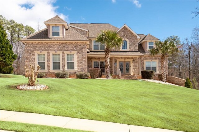 view of front of home featuring a shingled roof, a front lawn, and brick siding