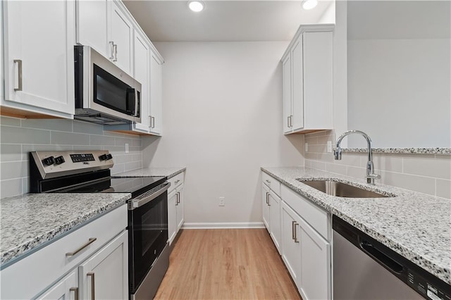 kitchen with appliances with stainless steel finishes, light stone counters, white cabinetry, and sink