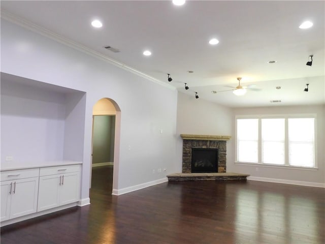 330 La Perla Dr, Sugar Hill, GA 30518 - unfurnished living room featuring a ceiling fan, arched walkways, ornamental molding, dark wood-style floors, and a stone fireplace