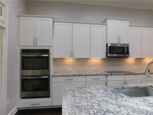 330 La Perla Dr, Sugar Hill, GA 30518 - kitchen with appliances with stainless steel finishes, white cabinets, backsplash, light stone countertops, and dark wood finished floors