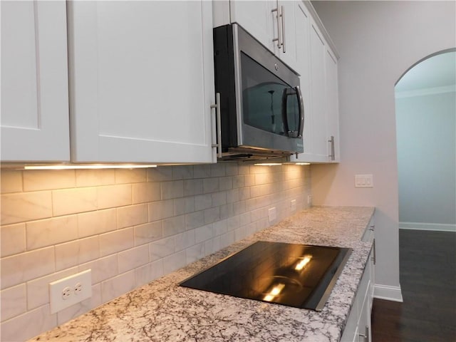 330 La Perla Dr, Sugar Hill, GA 30518 - kitchen with stainless steel microwave, black electric stovetop, arched walkways, white cabinets, and ornamental molding
