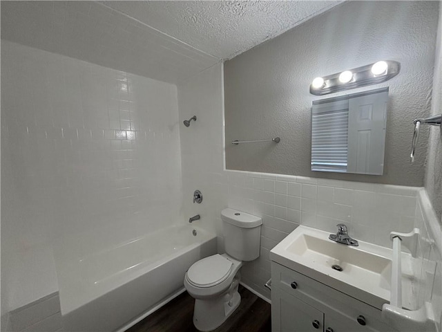 full bathroom featuring toilet, tile walls, a textured ceiling, vanity, and tiled shower / bath combo