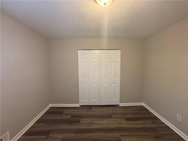 unfurnished bedroom with a textured ceiling, dark hardwood / wood-style flooring, and a closet