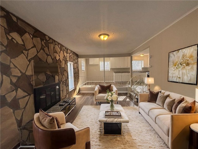 living room with crown molding, a stone fireplace, hardwood / wood-style floors, and a textured ceiling