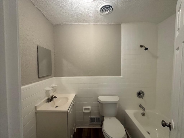 full bathroom with tile walls, vanity, a textured ceiling, toilet, and tiled shower / bath