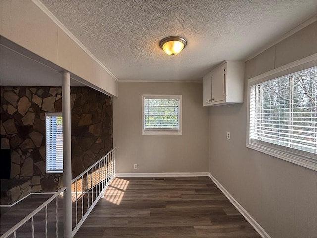 interior space featuring crown molding, a stone fireplace, dark hardwood / wood-style floors, and a textured ceiling