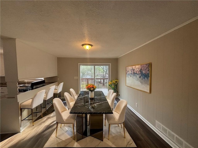 dining space with wood-type flooring, ornamental molding, and a textured ceiling