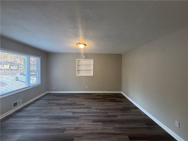 spare room with built in shelves, dark hardwood / wood-style floors, and a textured ceiling