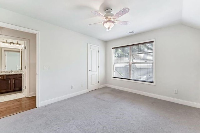 unfurnished bedroom with lofted ceiling, sink, ensuite bath, ceiling fan, and light colored carpet