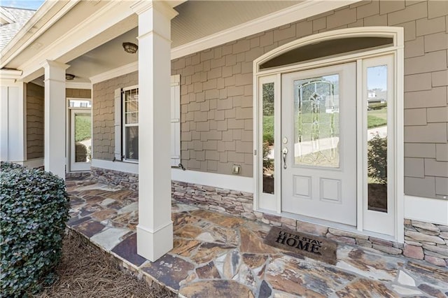 view of exterior entry featuring covered porch and roof with shingles