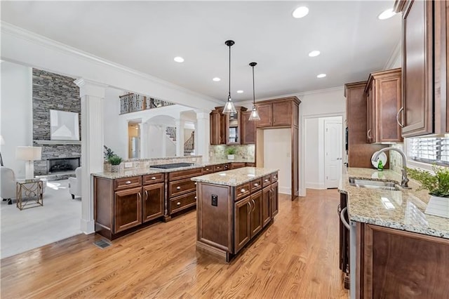 kitchen featuring sink, a center island, a stone fireplace, light hardwood / wood-style flooring, and decorative light fixtures